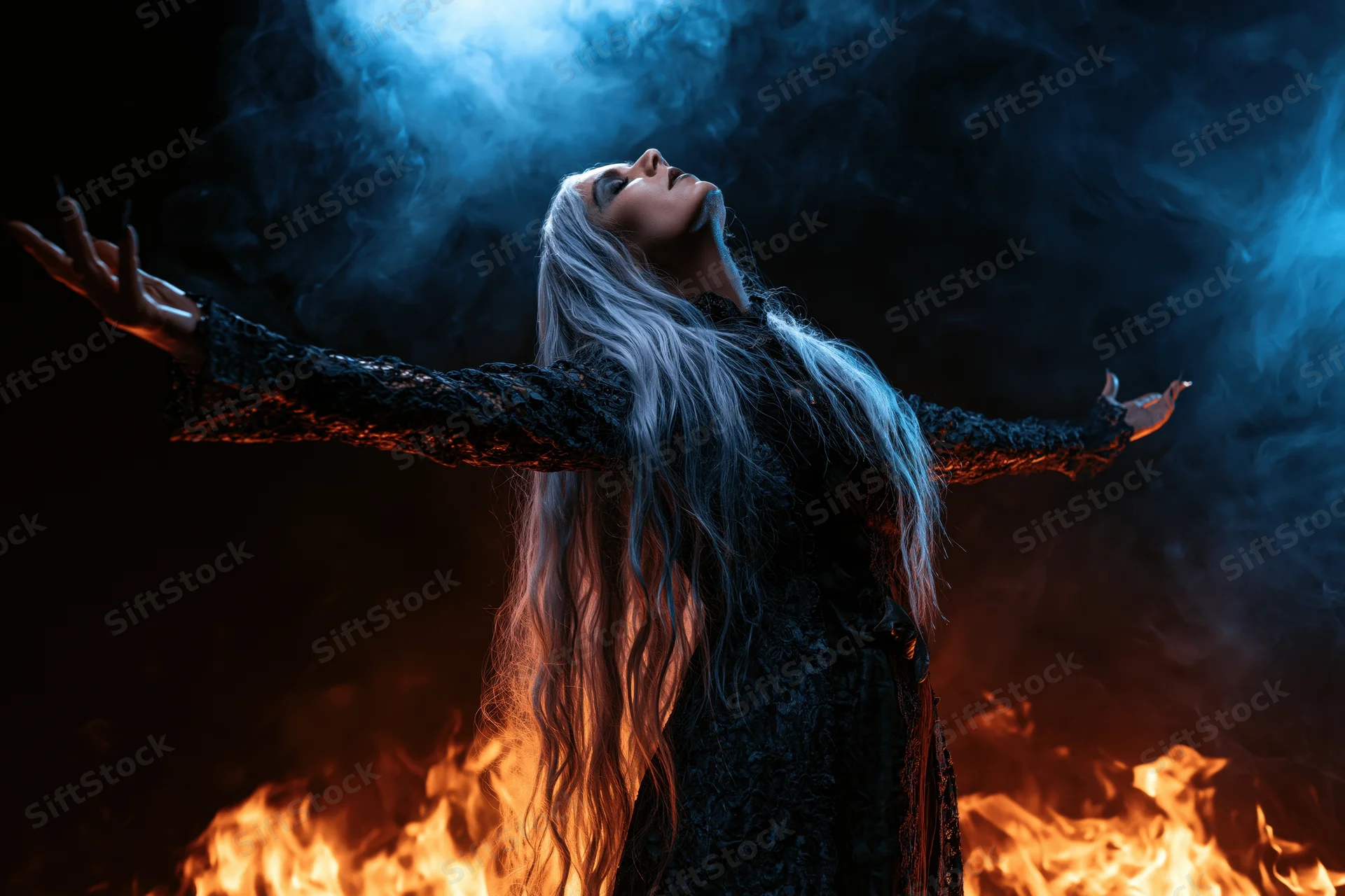 Woman with long silver-white hair standing arms outstretched amidst flames and smoke in dark mystical setting