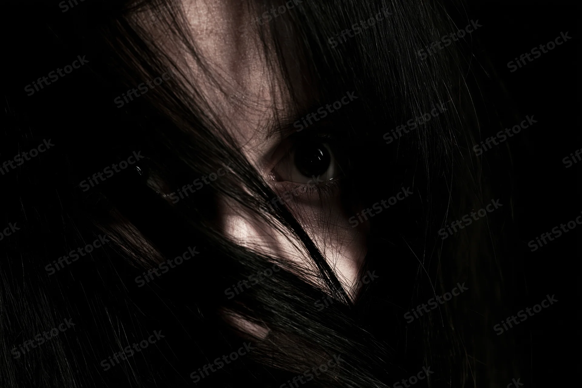 Woman's eye visible through long black hair in dark closeup portrait