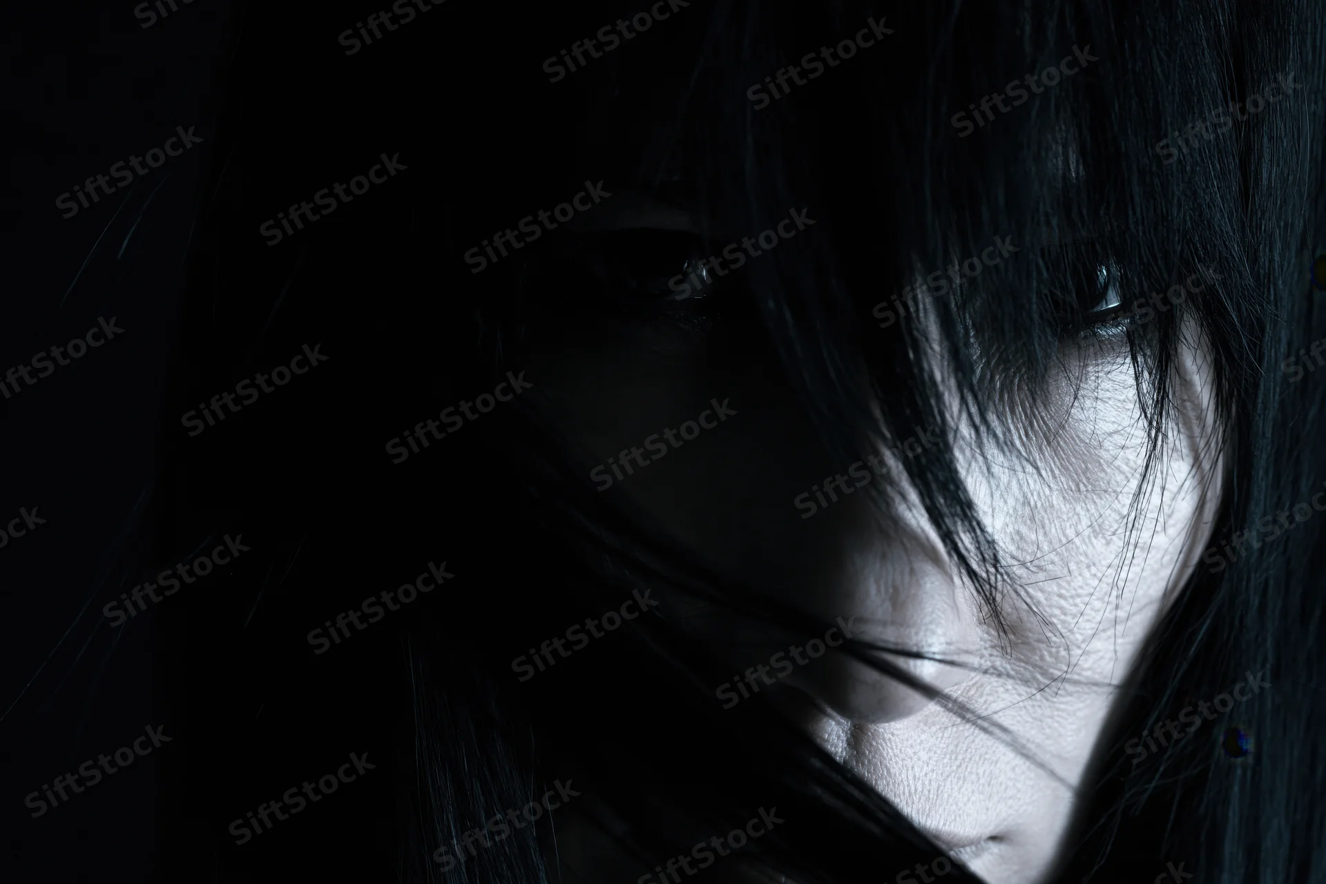 Woman's face partially hidden by long black hair in dramatic shadowed closeup