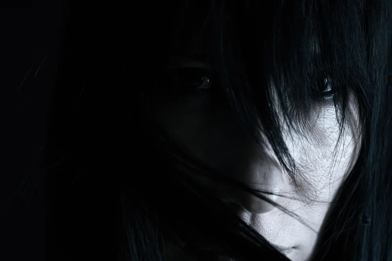 Woman's face partially hidden by long black hair in dramatic shadowed closeup