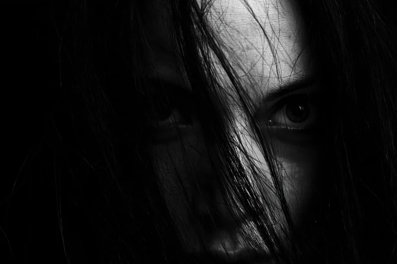 Woman’s face partially obscured by long black hair in dramatic closeup