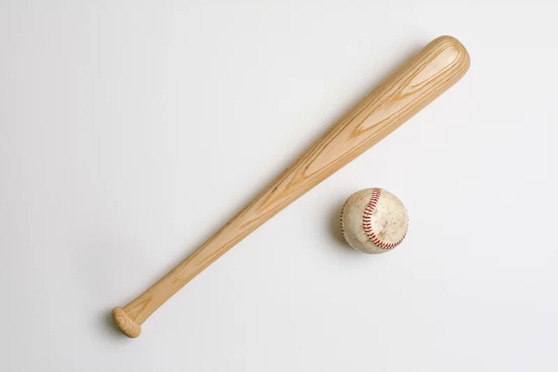 Wooden baseball bat and worn leather baseball arranged diagonally on white background