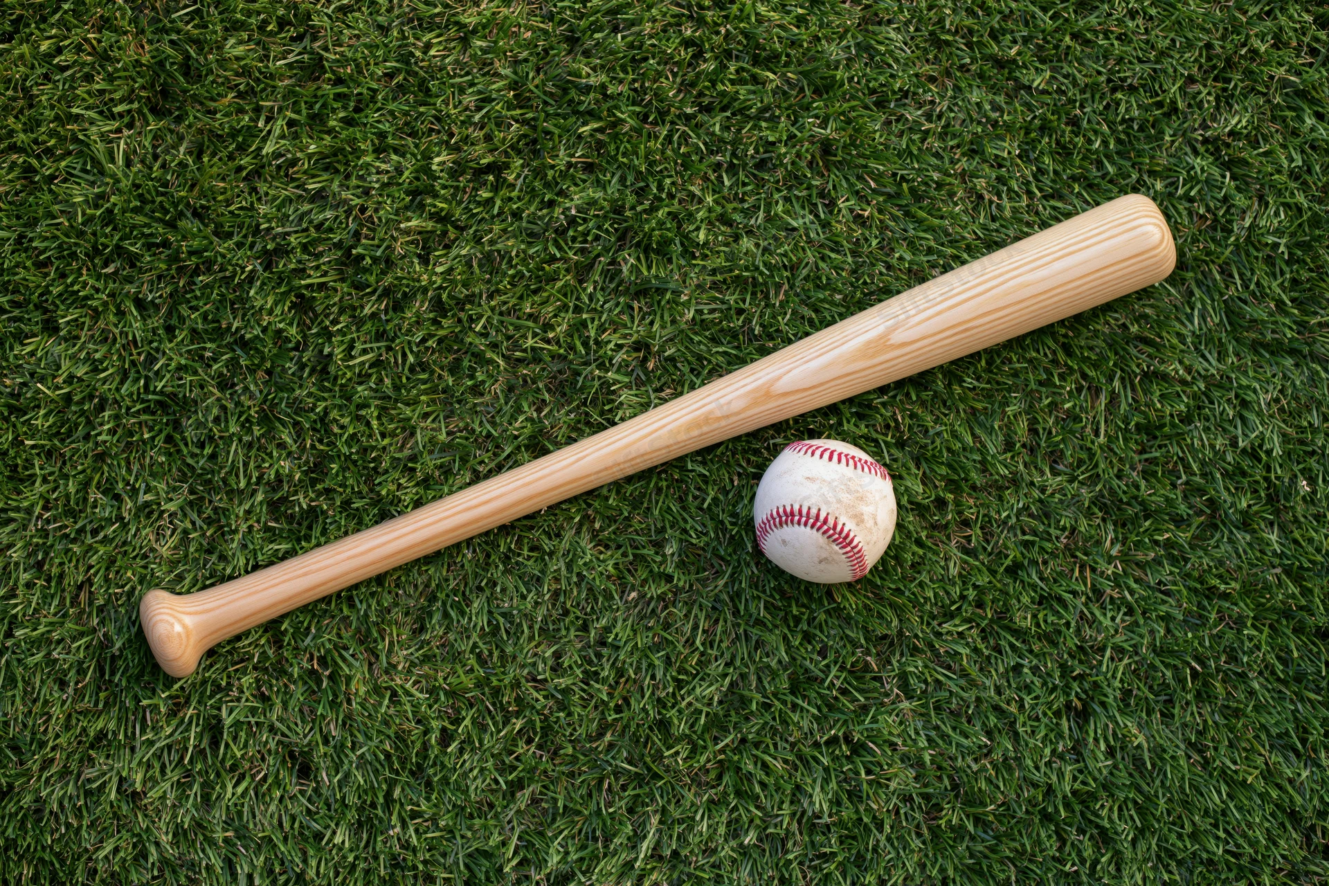 Wooden baseball bat and ball resting on green grass field