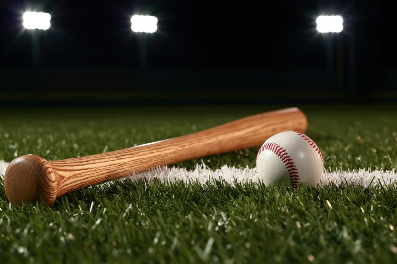 Wooden baseball bat and ball resting on green turf field under stadium lights at night