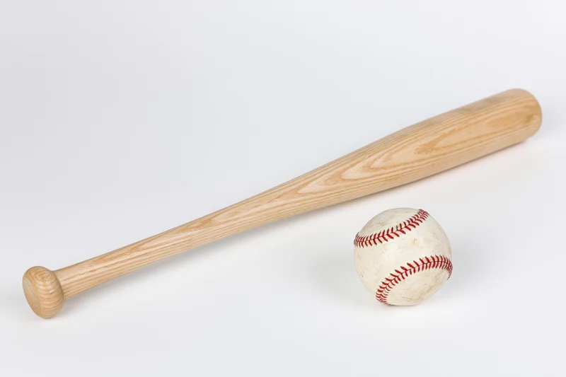 Wooden baseball bat resting diagonally beside a white leather baseball on a plain white surface