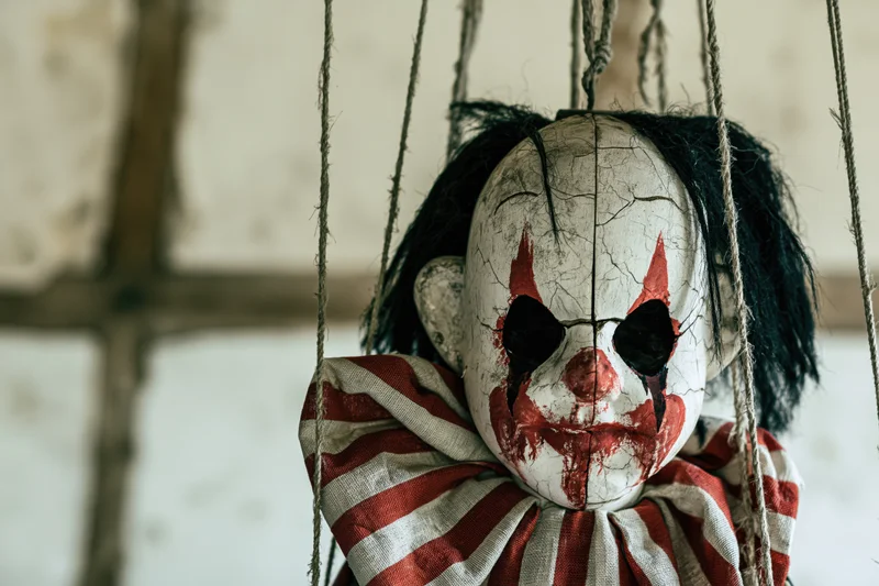 Worn creepy clown marionette doll hanging from frayed rope strings indoors