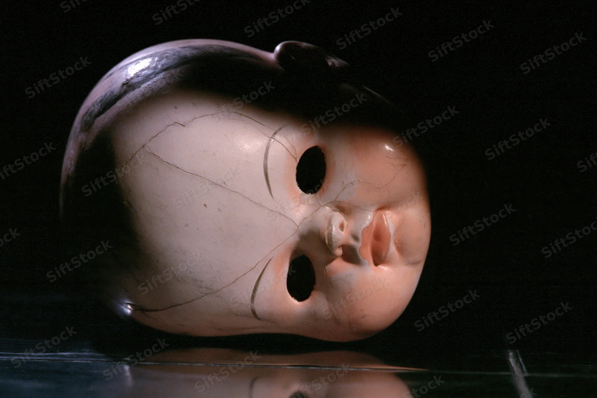 Cracked plastic doll head lying on its side on a dark reflective surface