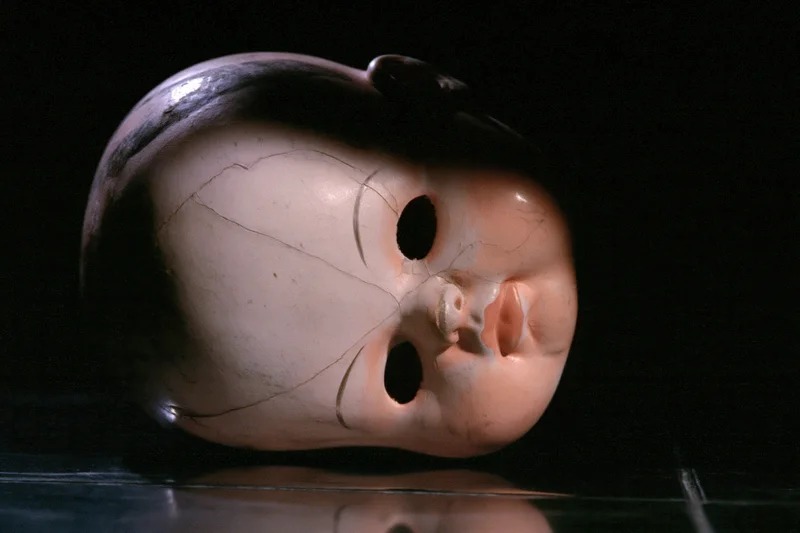 Cracked plastic doll head lying on its side on a dark reflective surface