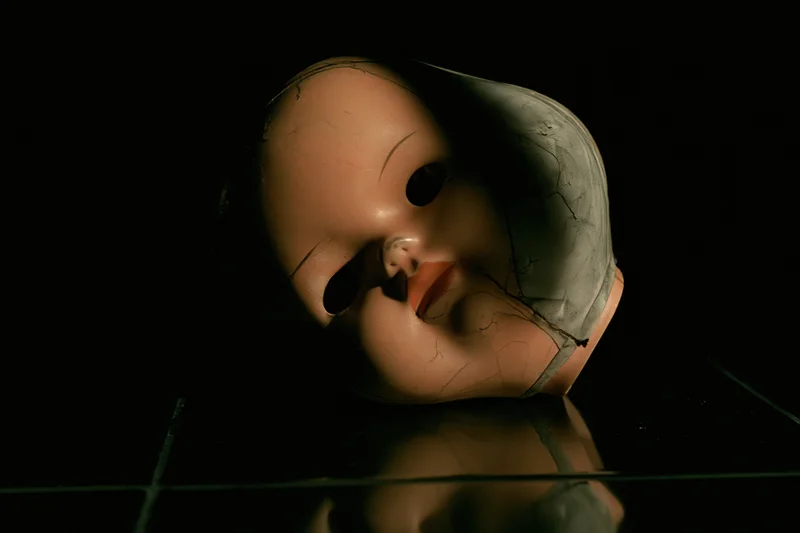 Worn plastic doll head lying on its side on a dark reflective surface