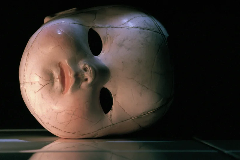 Cracked plastic doll head resting on a dark reflective surface