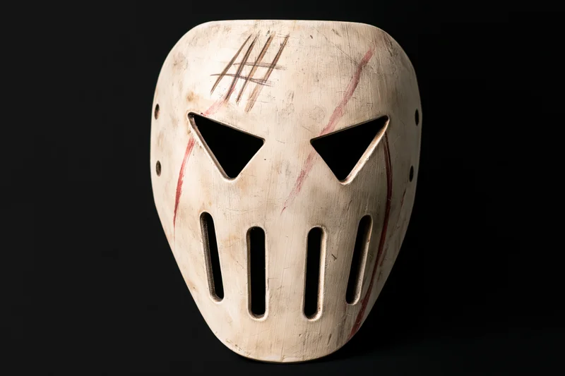 Worn white hockey-style face mask with angular eye cutouts and vertical slats on black background