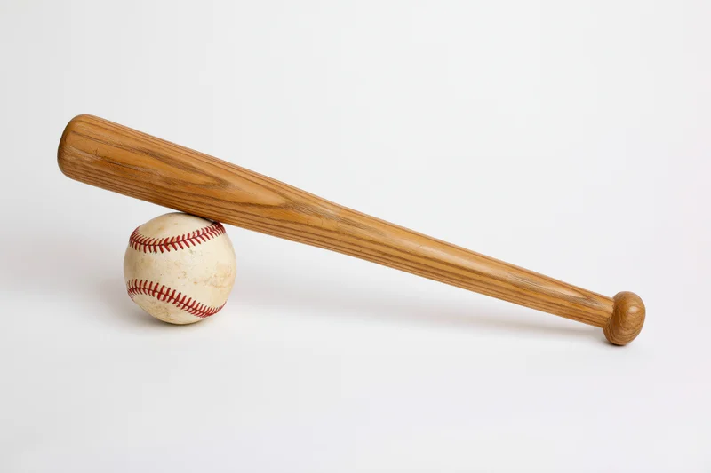 Wooden baseball bat resting diagonally across a white background with a worn baseball underneath