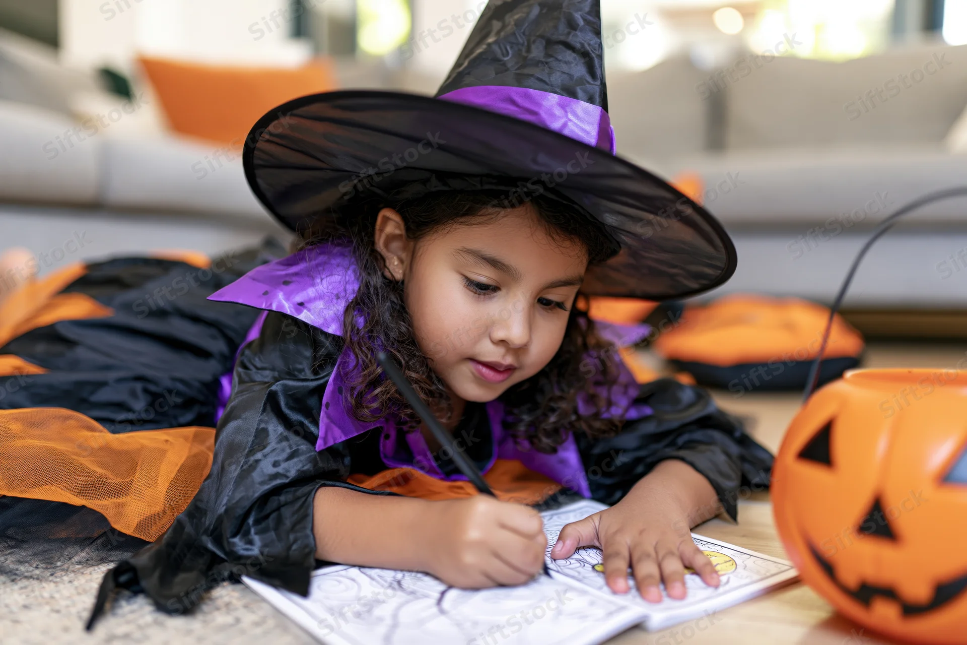 Young latina girl in witch costume coloring a book on the floor at home