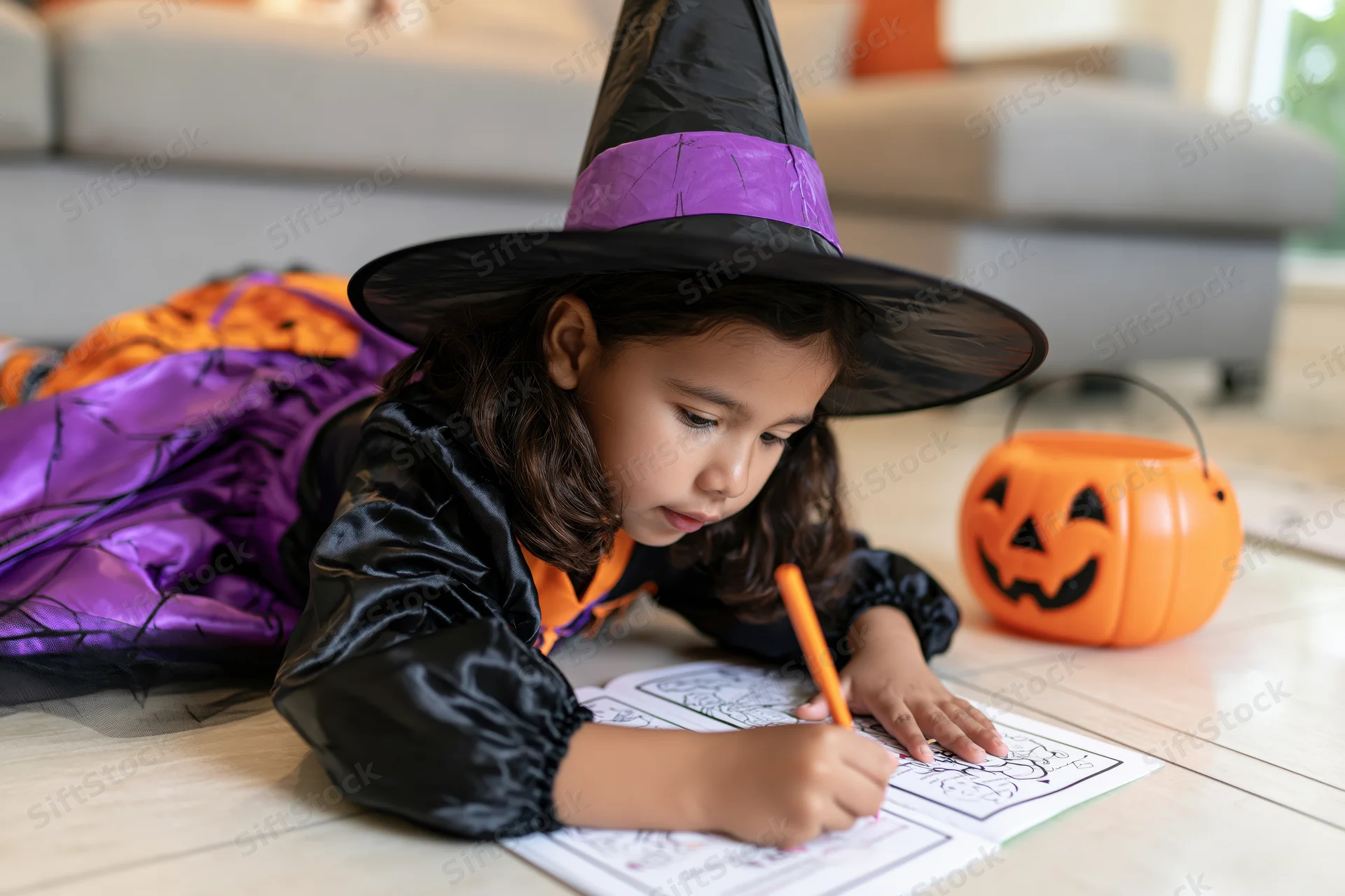 Young latina girl in witch costume coloring on floor at home