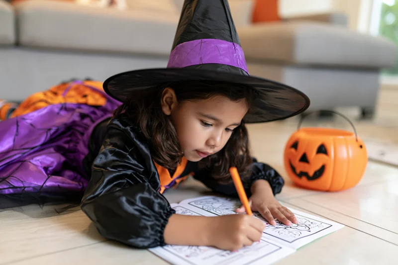 Young latina girl in witch costume coloring on floor at home