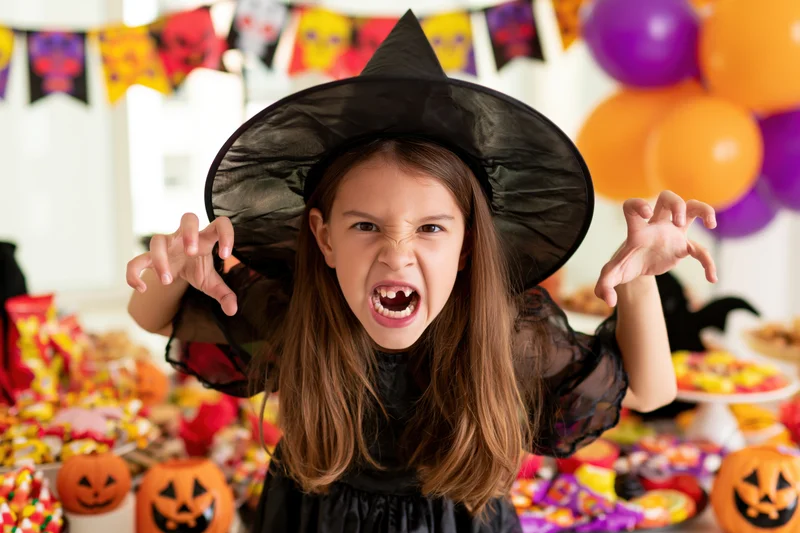 Young girl in witch costume making angry face with fangs at halloween party