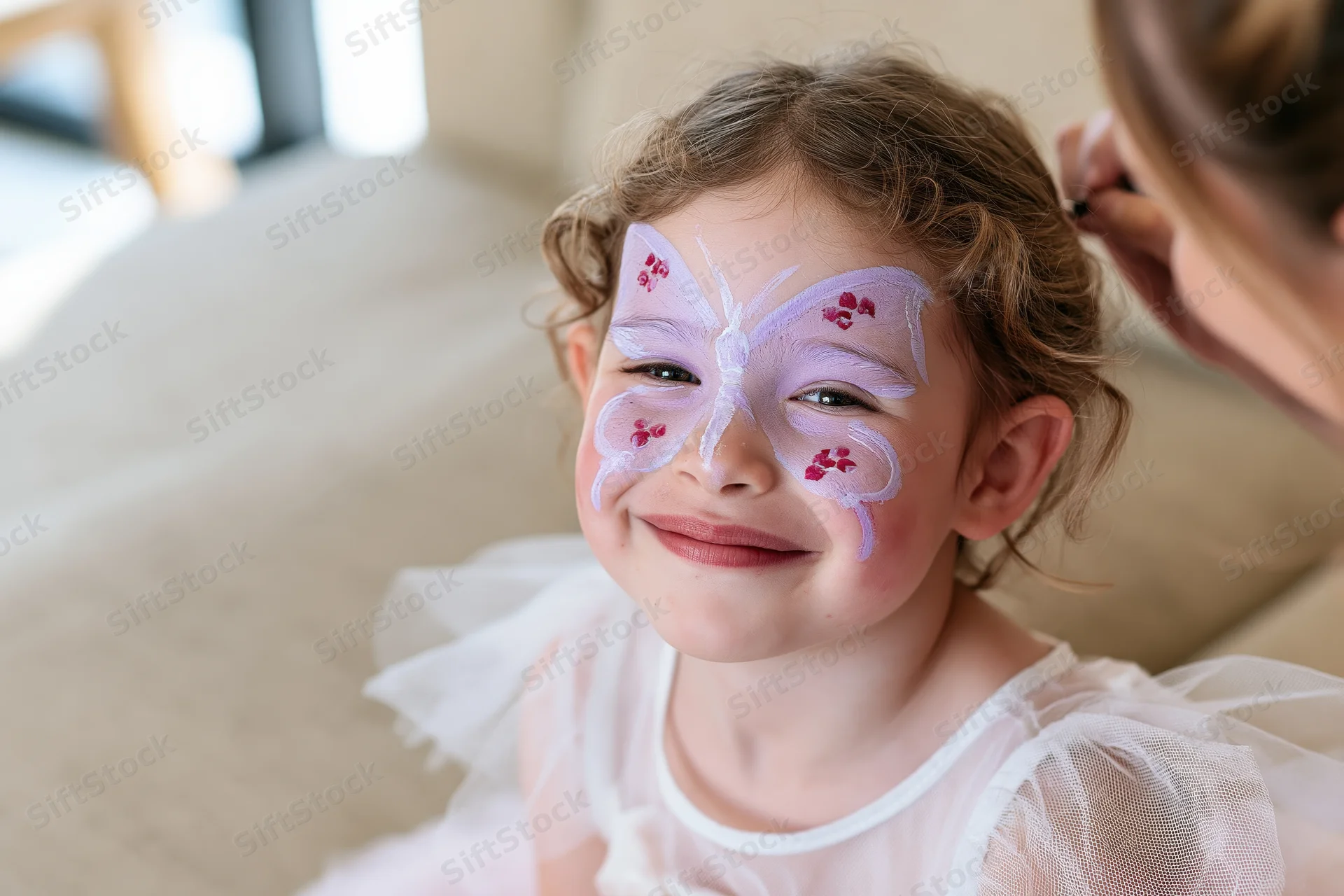 Young girl smiling with butterfly face paint while an adult applies makeup at home