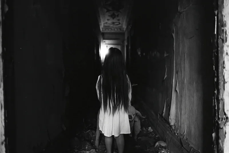 Girl in white dress walking down dark abandoned hallway with long hair covering her face