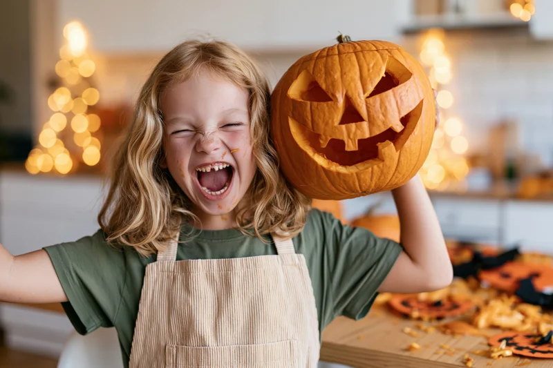 Young girl laughing with carved pumpkin in kitchen during halloween crafting