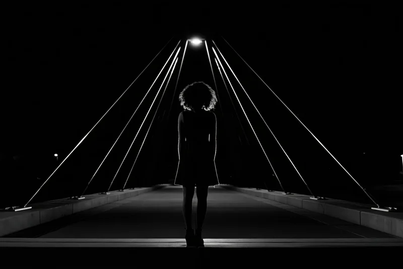 Silhouette of a woman standing still at the center of a cable-stayed pedestrian bridge at night