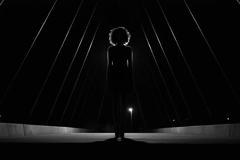 Silhouette of a woman standing still at the center of a pedestrian bridge at night