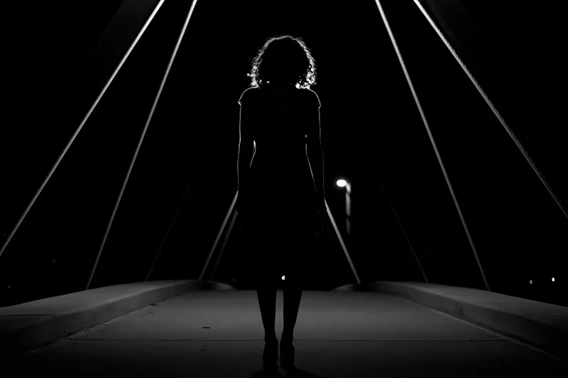 Silhouette of a young woman standing still at the center of a pedestrian bridge at night