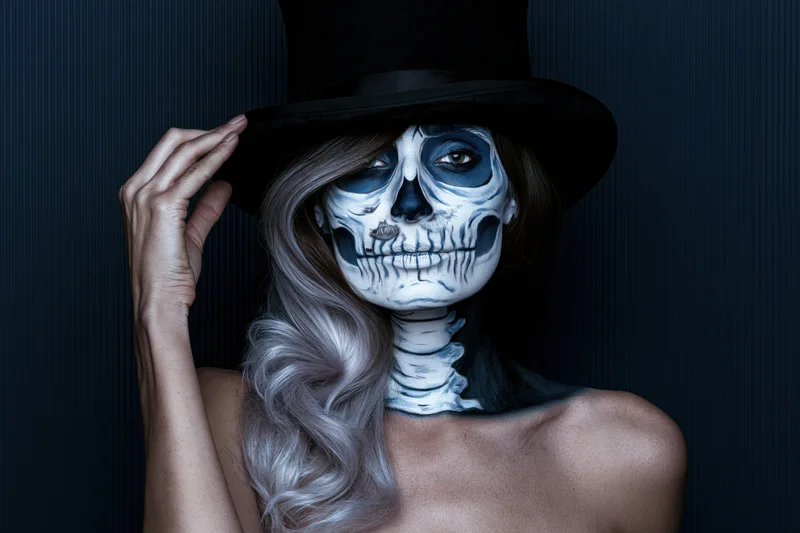 Woman with skeleton face paint and top hat posing against dark background