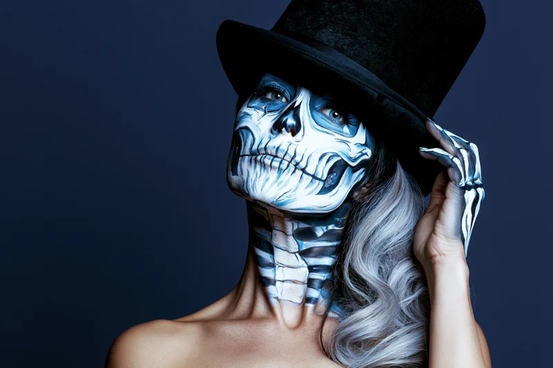 Woman with skeleton face paint and top hat posing against dark background