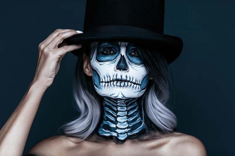 Woman with skeleton face paint and top hat posing against dark background