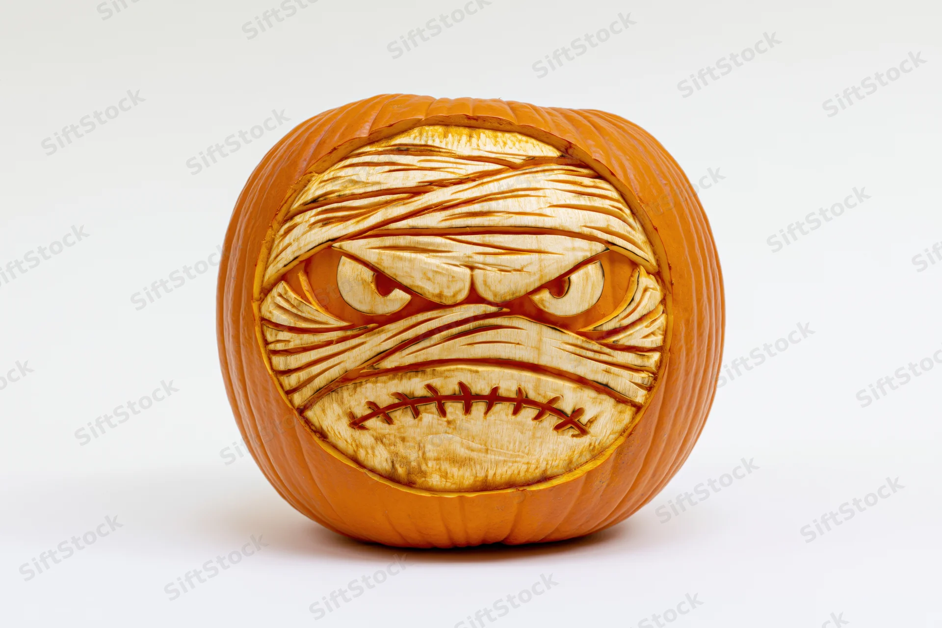 Carved pumpkin with mummy face and woodburned details on white background