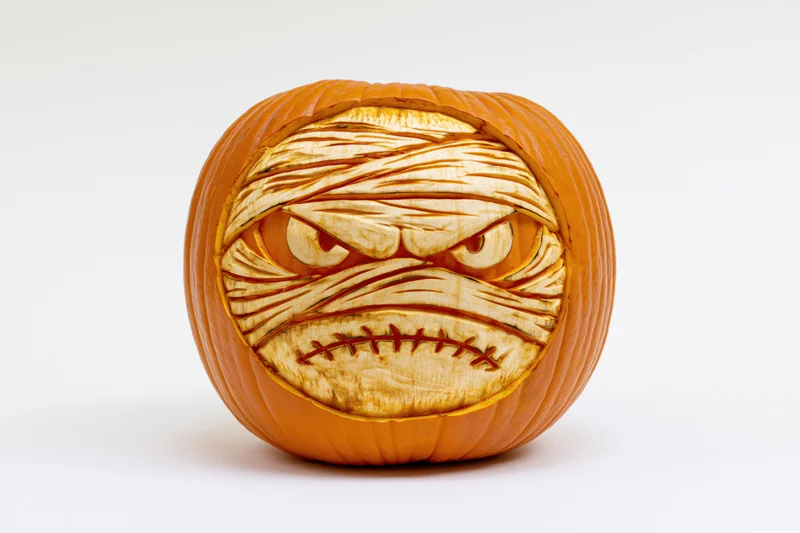Carved pumpkin with mummy face and woodburned details on white background