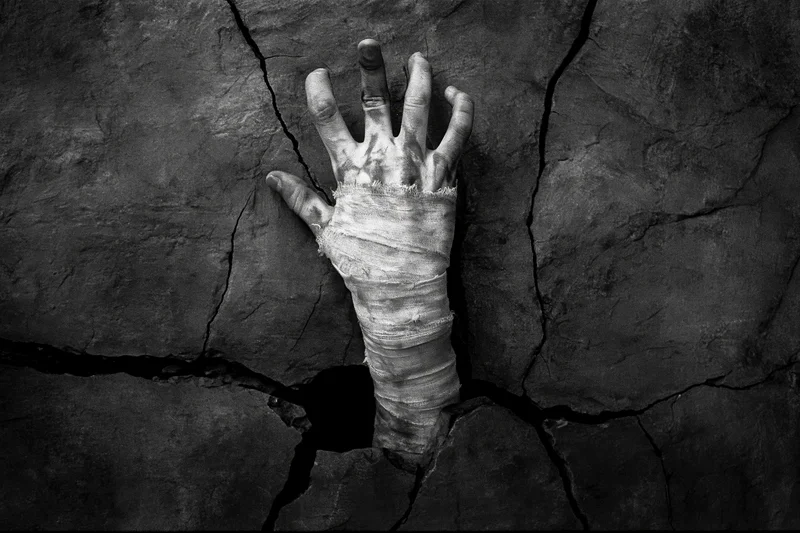 Bandage-wrapped hand reaching up through a crack in stone