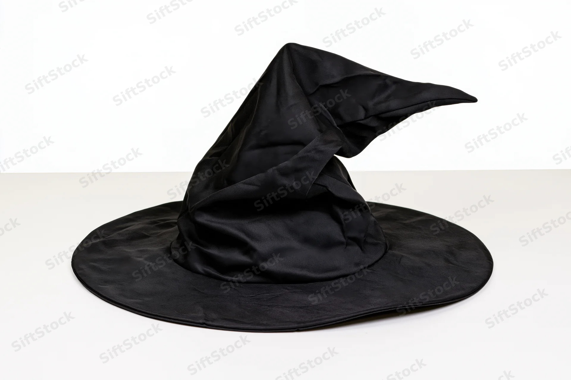 Black witch hat with floppy pointed crown resting on white surface