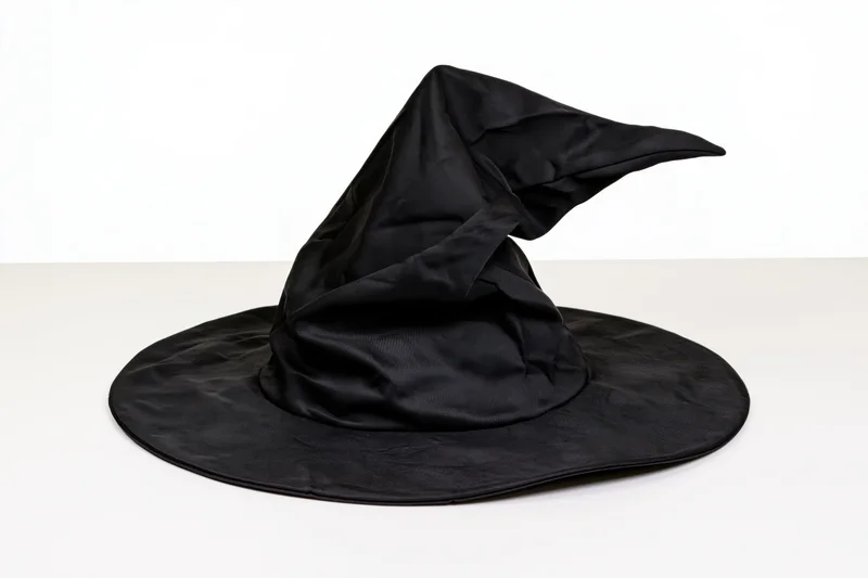 Black witch hat with floppy pointed crown resting on white surface