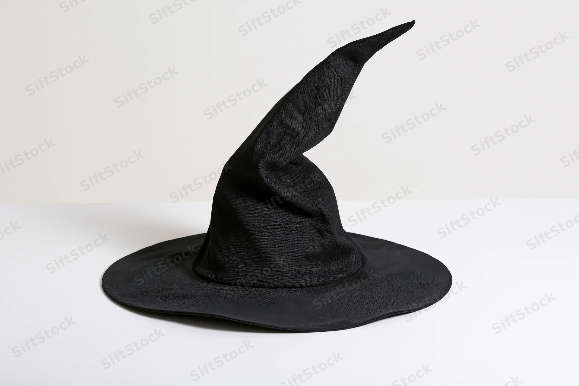 Black fabric witch hat with crooked pointed crown on white surface