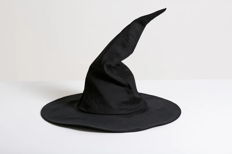 Black fabric witch hat with crooked pointed crown on white surface