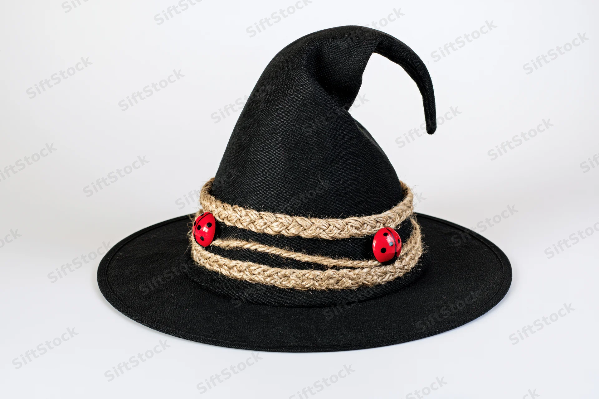 Black fabric witch hat with curved point and twine band decorated with red ladybug buttons on white background