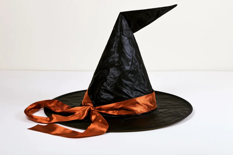 Black witch hat with orange satin ribbon on white surface