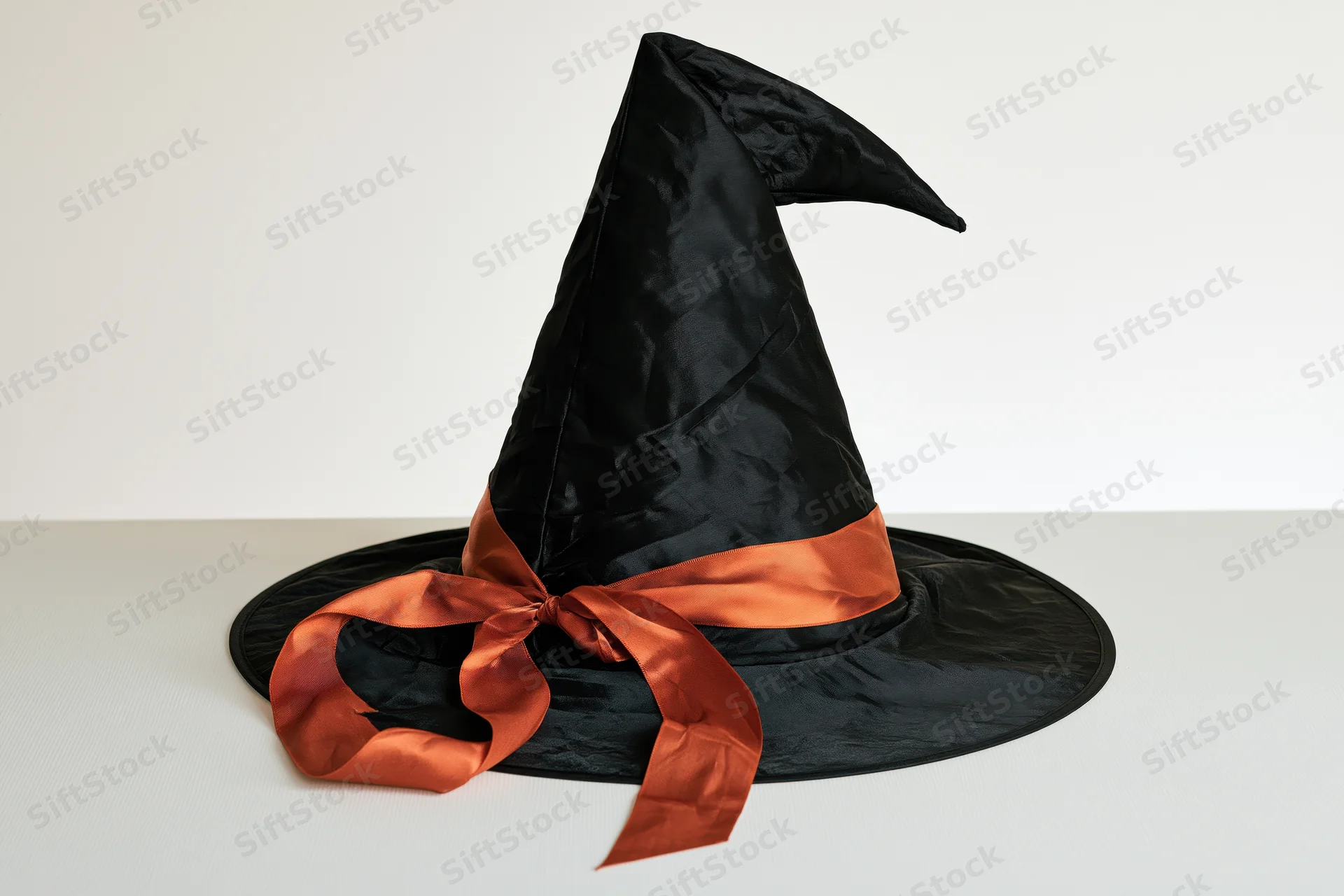 Black witch hat with orange ribbon on white surface