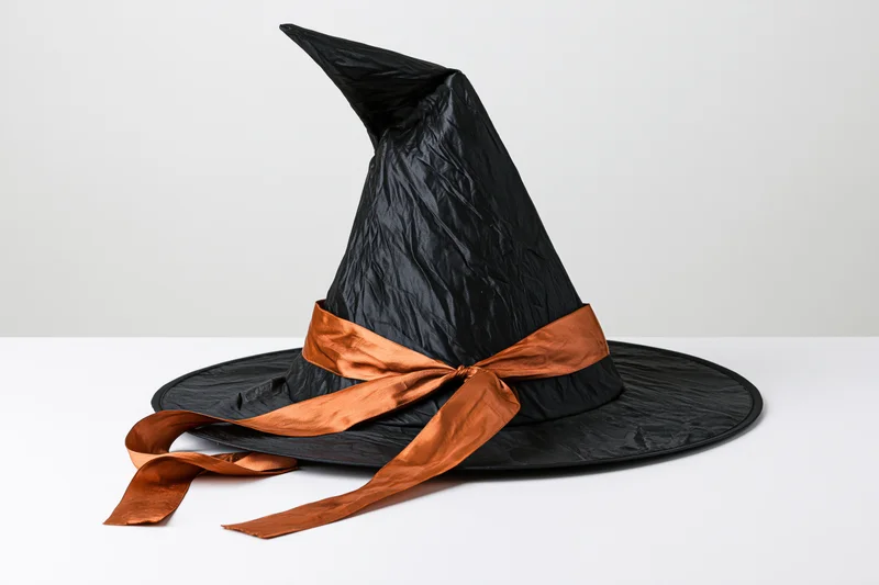 Black witch hat with orange ribbon on white surface