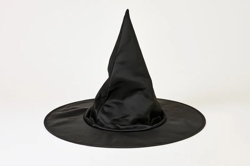 Black pointed witch hat resting on white surface, slightly crumpled fabric, isolated against plain background