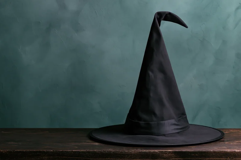Black pointed witch hat resting on wooden table against teal textured wall