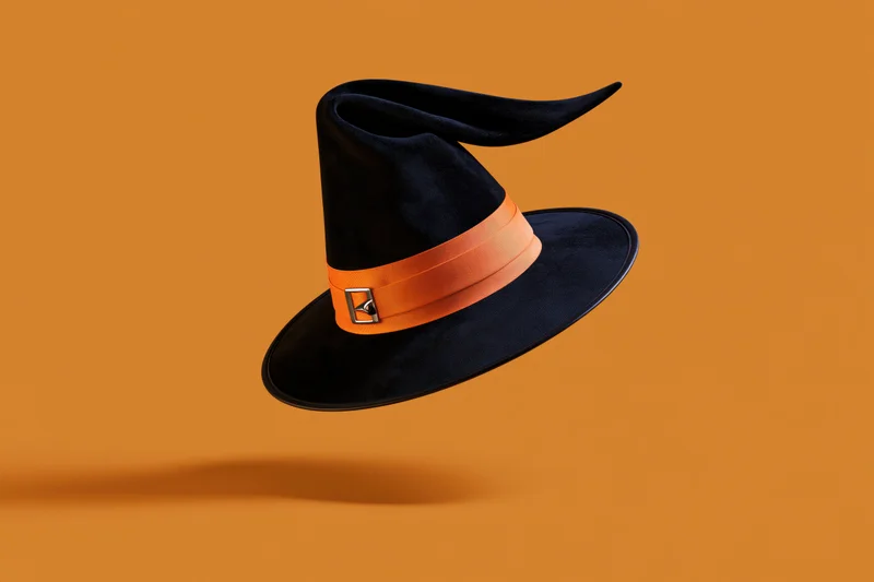 Black witch hat with orange ribbon and silver buckle floating against orange background