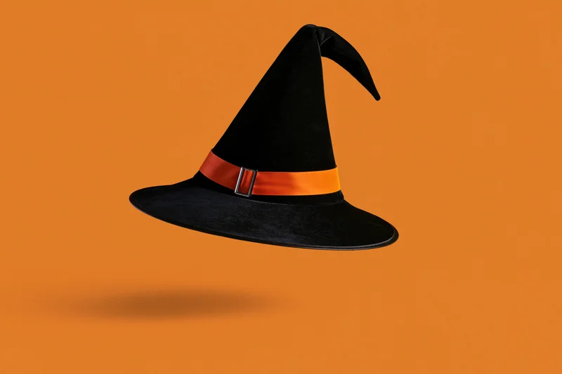 Black witch hat with orange ribbon and silver buckle floating against orange background