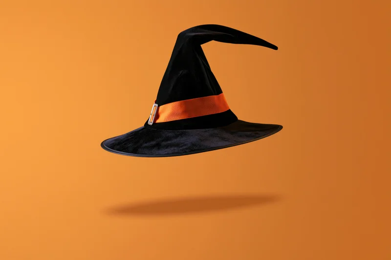 Black witch hat with orange ribbon and silver buckle floating against orange background