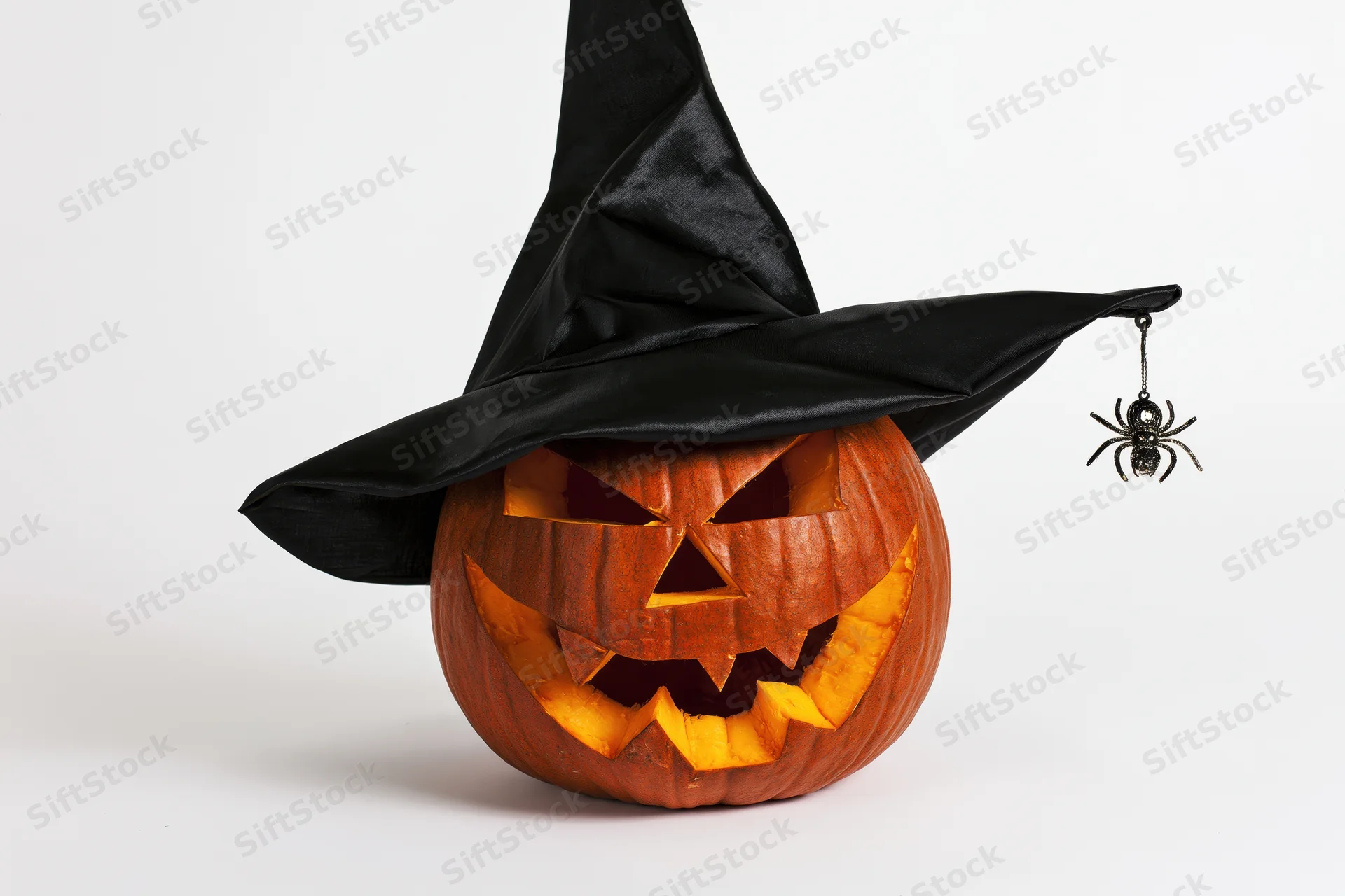 Carved jack-o-lantern wearing a witch hat with a spider hanging from the brim on a white background