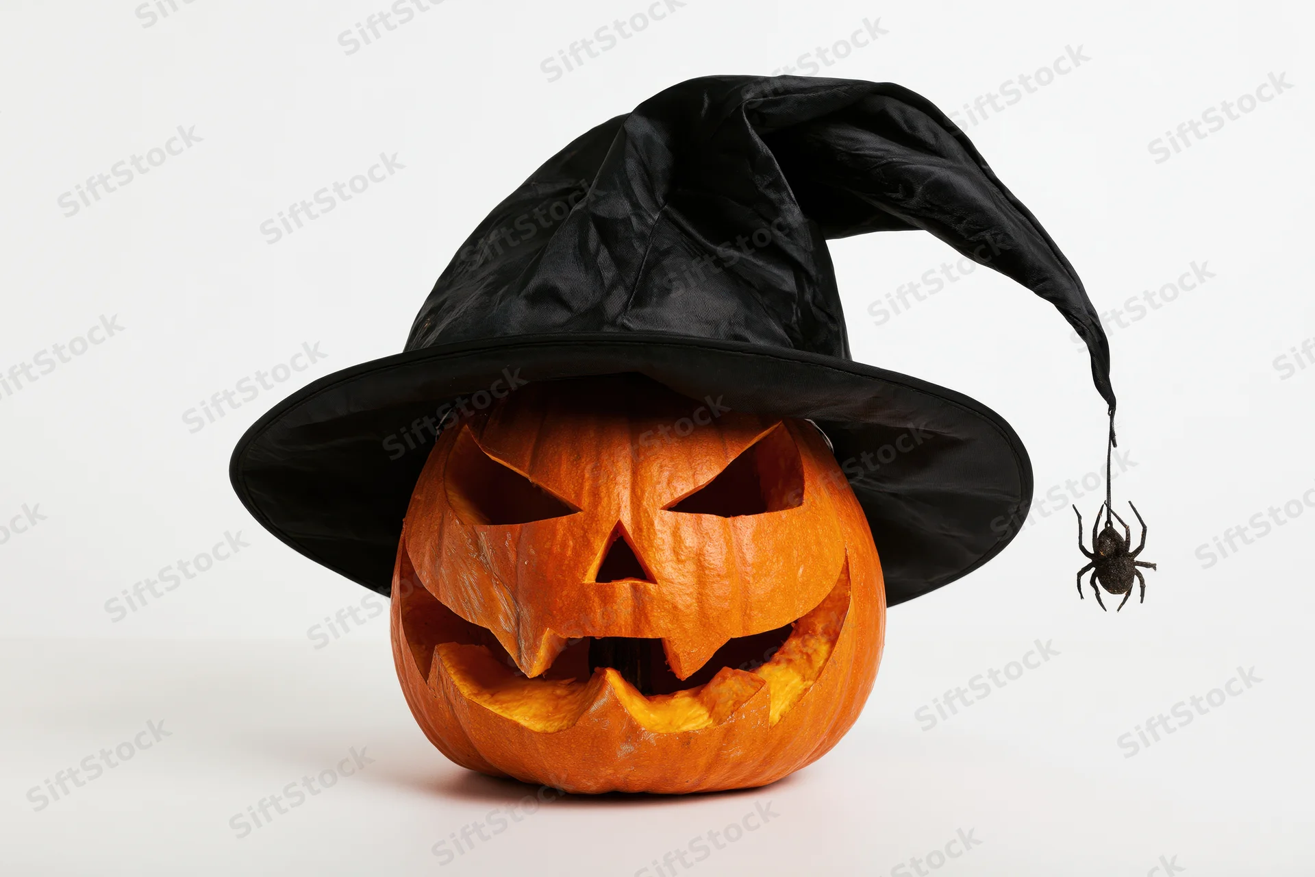 Carved pumpkin wearing witch hat with spider decoration on white background