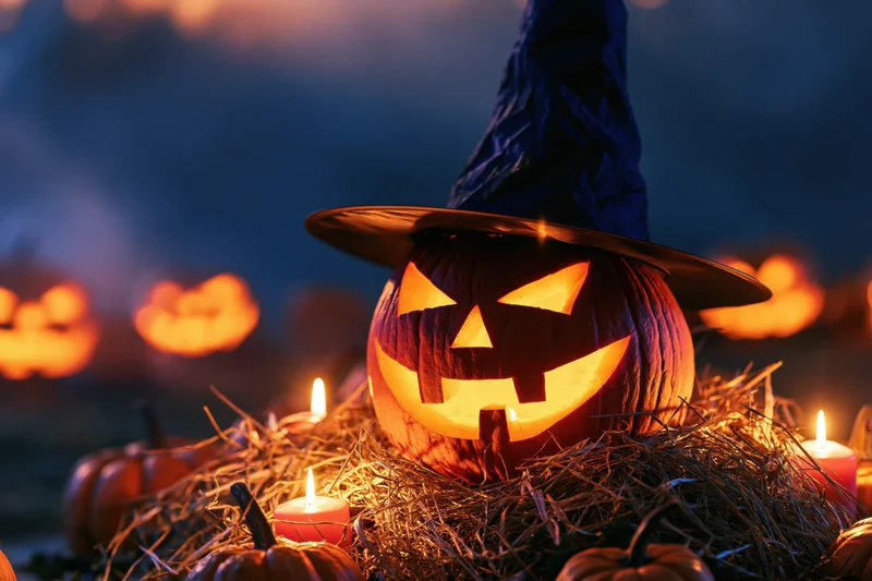 Carved jack-o-lantern wearing witch hat glowing on hay at night