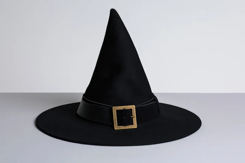 Black witch hat with tall pointed crown and wide brim on white surface
