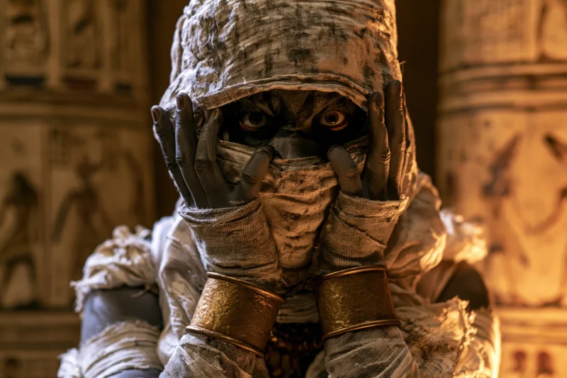 Costumed performer as ancient egyptian mummy with bandages and gold bracelets in tomb setting
